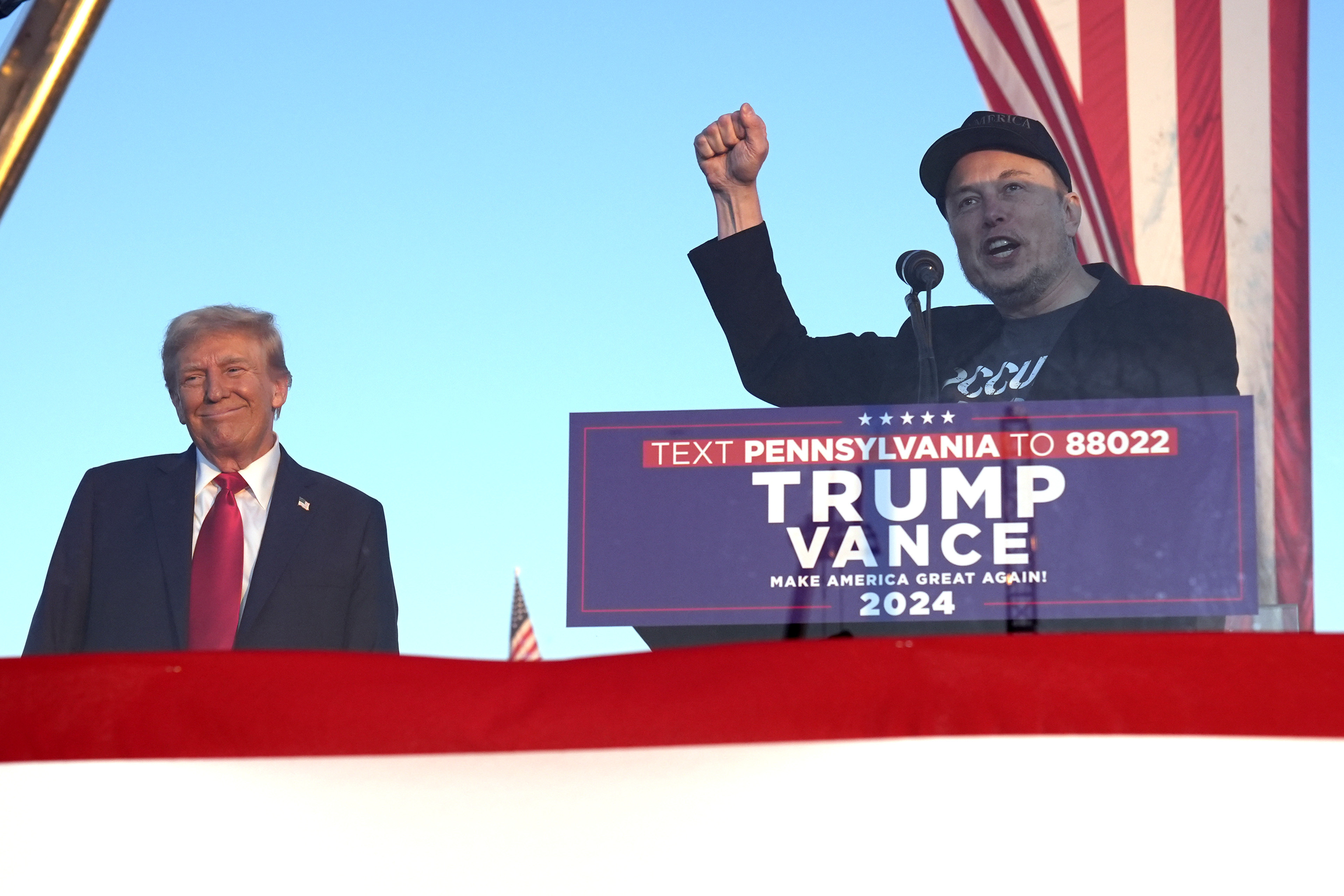Elon Musk speaks as Donald Trump listens at a campaign event. Elon Musk speaks as Donald Trump listens at a campaign event.